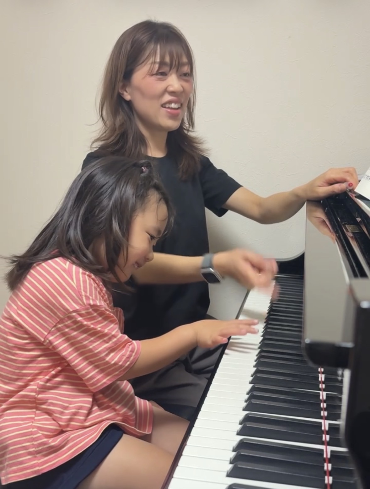 先生と笑顔で一緒にピアノを弾く子ども